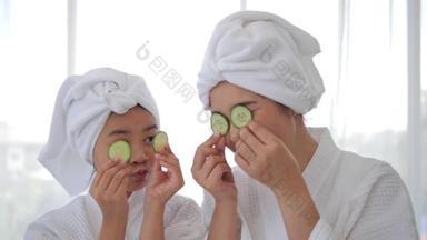 身穿白色浴衣的亚洲母亲和女儿把黄瓜放在有乐趣的眼睛上，看着相机。<strong>水</strong>疗美容程序在家里为女孩。护肤、<strong>保湿</strong>及<strong>保湿</strong>概念.